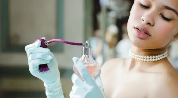 Elegancka kobieta w rękawiczkach aplikuje perfumy. Dowiedz się, jak sprawdzić oryginalność perfum, by cieszyć się pięknym zapachem.