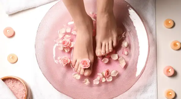 Relaks w domowym spa: stopy w różowej kąpieli z płatkami róż i świecami. To właśnie jest pedicure co to znaczy – dbanie o stopy.