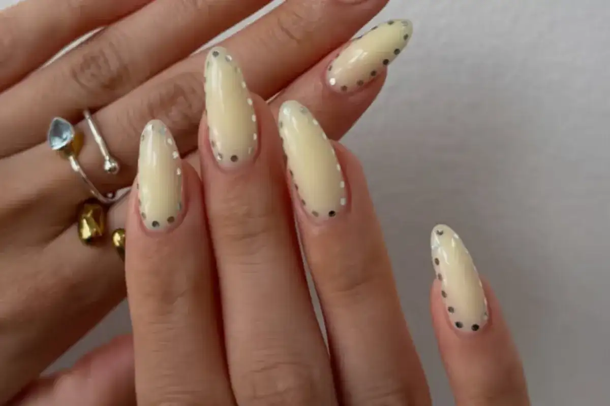 Modne paznokcie w jasnych kolorach, ozdobione srebrnymi kropkami. Delikatny, pastelowy manicure z błyszczącymi detalami.